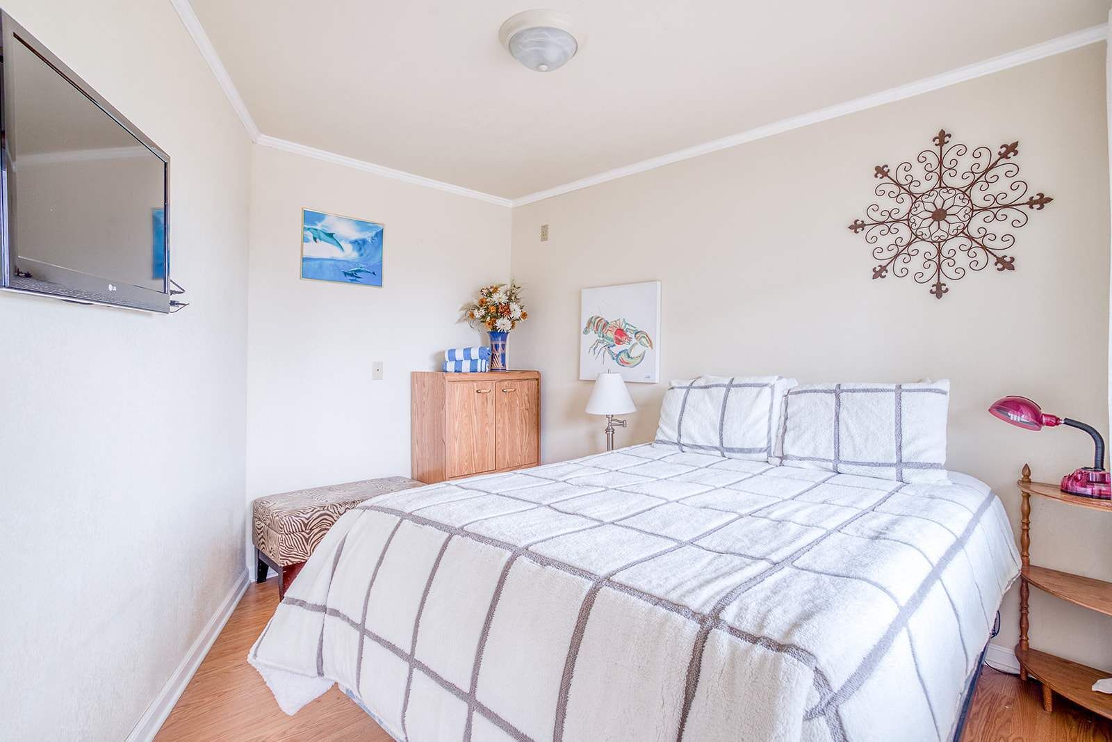 Une chambre à coucher comprenant un lit, une armoire en bois, un bureau avec une lampe et des œuvres d’art décoratives accrochées au mur.