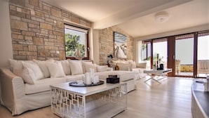 Amplia sala de estar con pared de piedra, un sofá blanco, una mesa de centro y vistas al exterior.