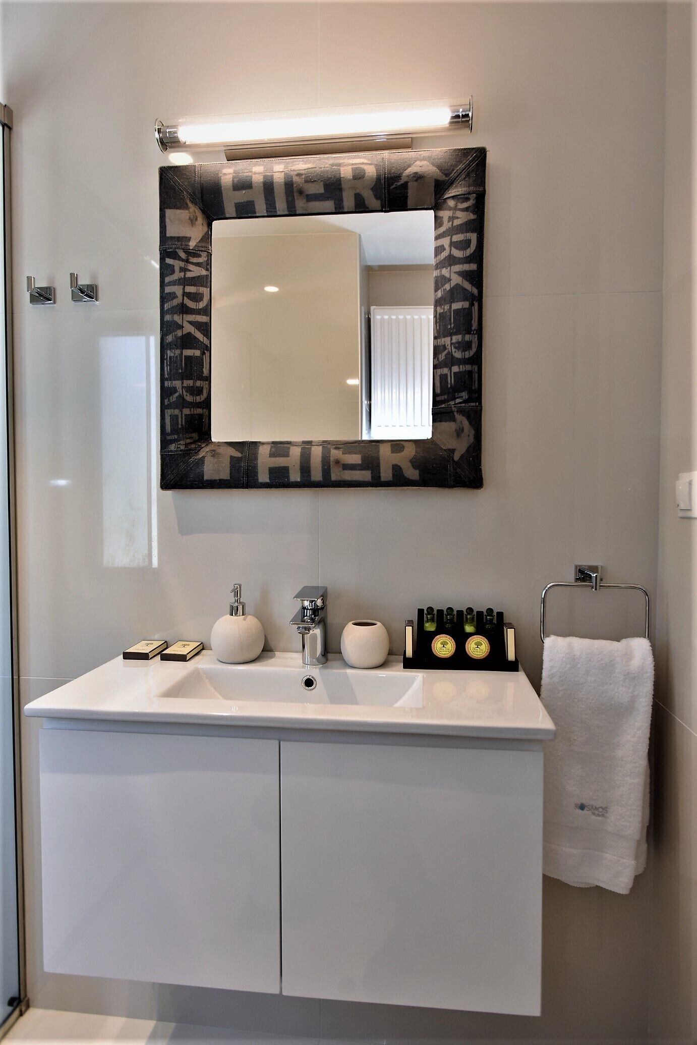 Un baño moderno con un espejo grande, un lavabo blanco y un perchero para toallas.