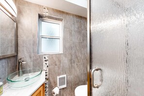 Een badkamer met een glazen wastafel, een raam, een toilet en een douche.
