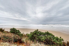 Een strand met golven, zand en groene begroeiing.
