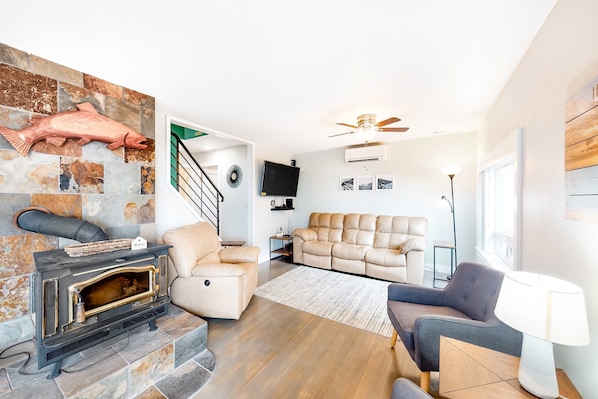 A living room with a stone fireplace, a sofa, a chair, and a TV. - Charming Ocean View Home with Free WiFi and Private Washer Dryer Dogs Welcome (Oceanside)