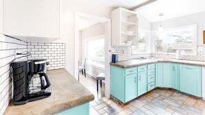 Une cuisine moderne équipée d’une machine à café, de meubles de couleur turquoise et d’une grande fenêtre.