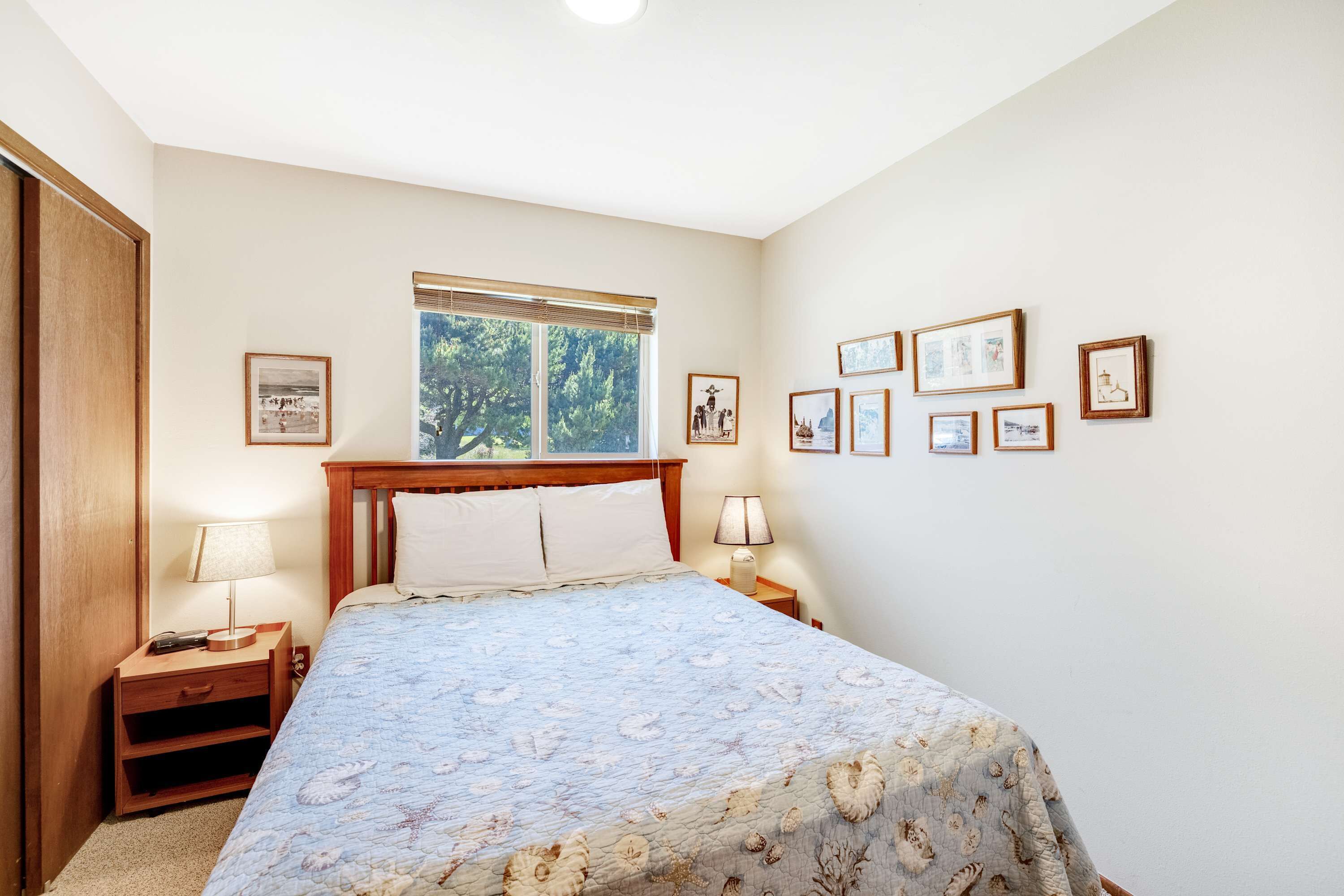 A bedroom with a bed, two bedside tables, a window, and several framed pictures on the wall.
