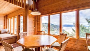 A wooden cabin with a large dining table, multiple chairs, and a view of the mountains through large windows. - Hand Built Gem with Two Large Decks and Incredible Views 1 4 Mile to the Beach (Oceanside)