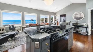 Een moderne keuken met een groot eiland, ingebouwde apparatuur en grote ramen met uitzicht op zee.