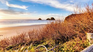 Een strand met rotsachtige rotsformaties en dichte begroeiing op de voorgrond.