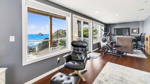 Een moderne woonkamer met grote ramen, een leren fauteuil, een loopband en uitzicht op de oceaan.