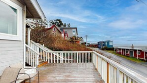 A wooden deck with a white railing, a chair, and a staircase leading to a house with a red roof and white trim.