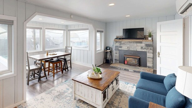 A spacious living room with a fireplace, a dining area with a table and chairs, and a blue sofa.