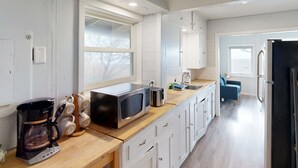 A modern kitchen with white cabinets, a wooden countertop, a coffee maker, a microwave, and a refrigerator.