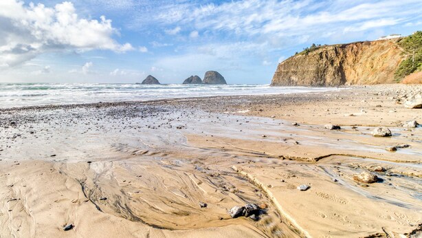 Una spiaggia con un litorale roccioso, onde e formazioni rocciose in lontananza.