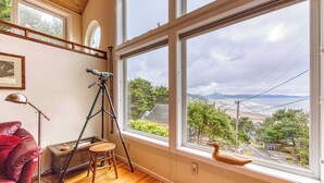 Une pièce dotée de grandes fenêtres, d’un télescope, d’un canapé en cuir rouge et d’un tabouret en bois.