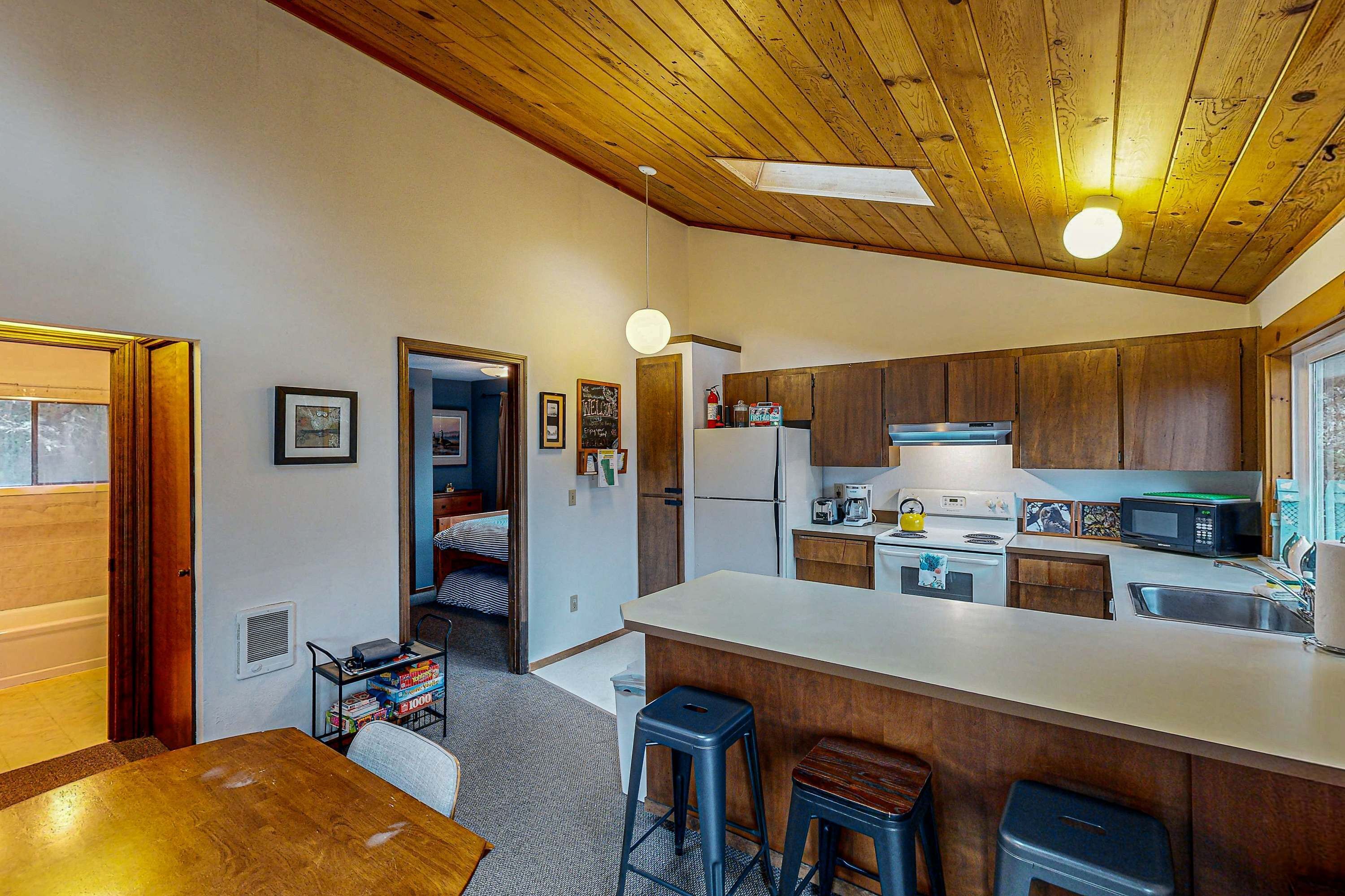 A modern kitchen with wooden cabinets, a large island, and a dining area with a wooden table and bar stools.