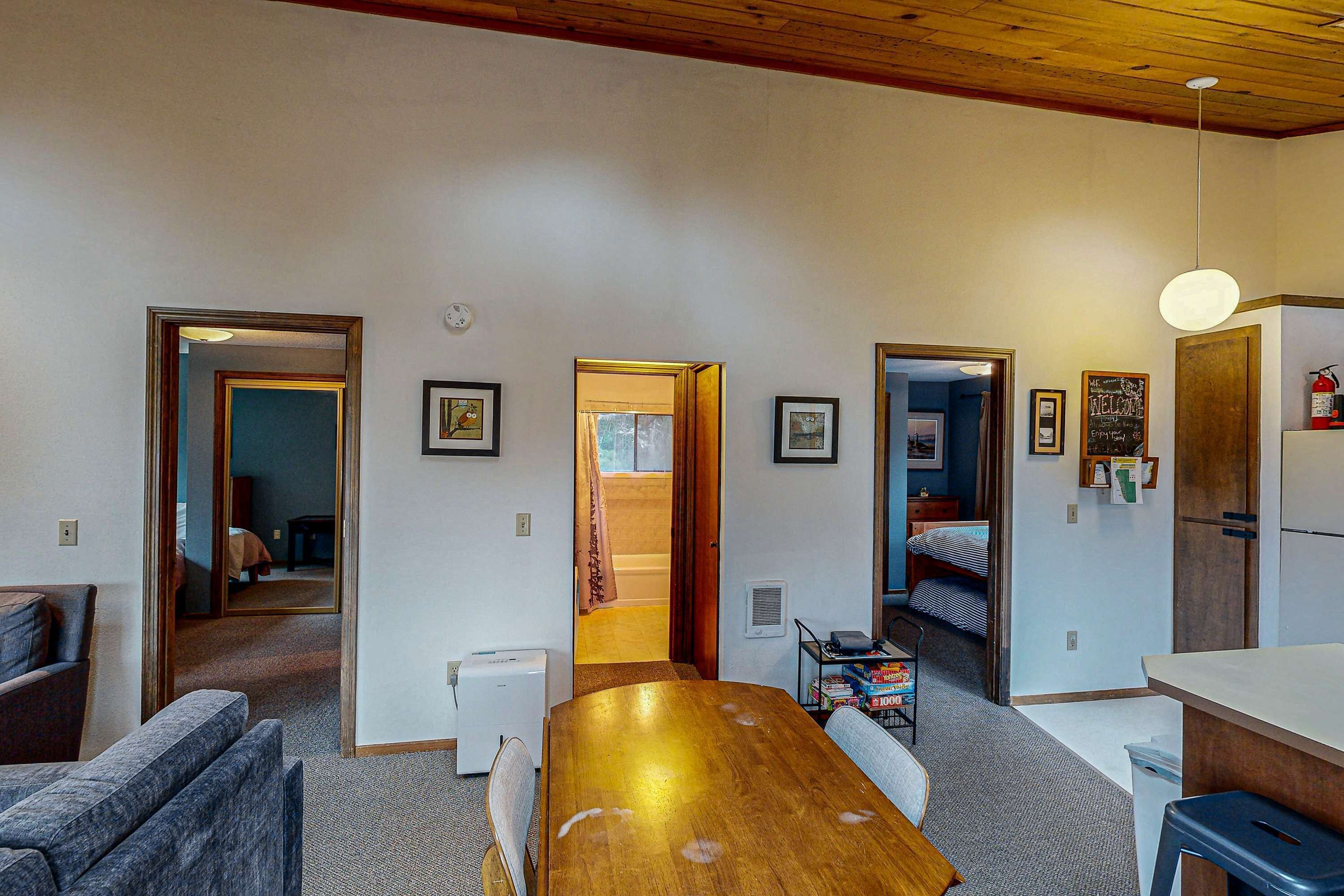 A compact living space with a wooden dining table, a sofa, a kitchenette, and a small bathroom visible through an open door.