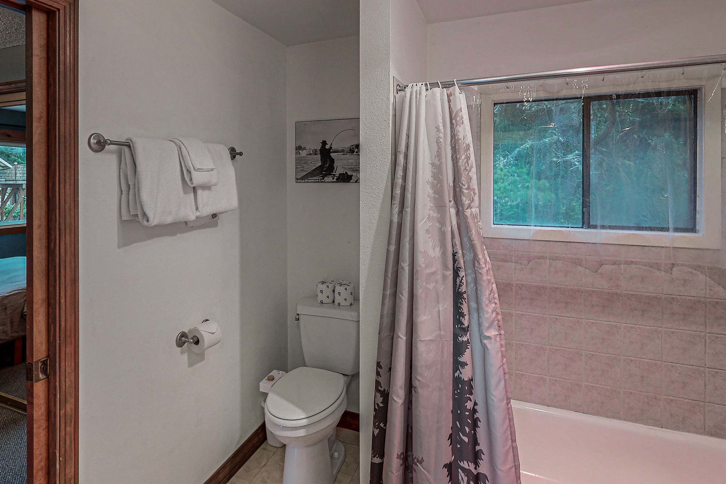 Et badeværelse med toilet, håndklædestang, bruseforhæng og et vindue.
