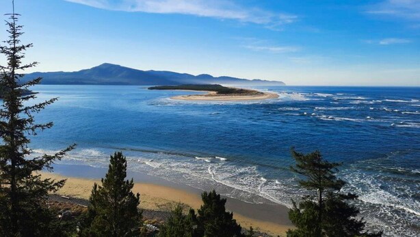 Un paisaje costero con playa, olas del océano y montañas a lo lejos.