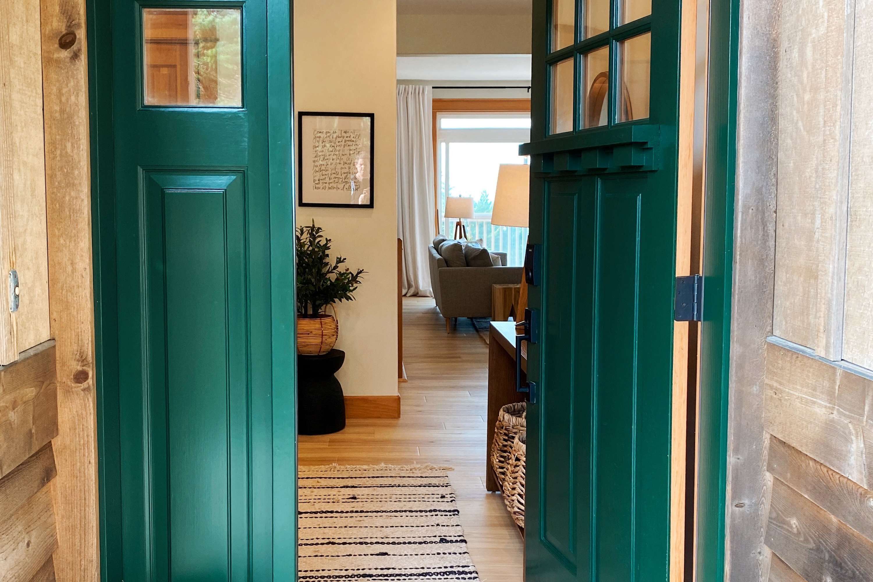 Un pasillo con una puerta verde azulada, paredes de madera, una planta en maceta, un sofá y una lámpara.