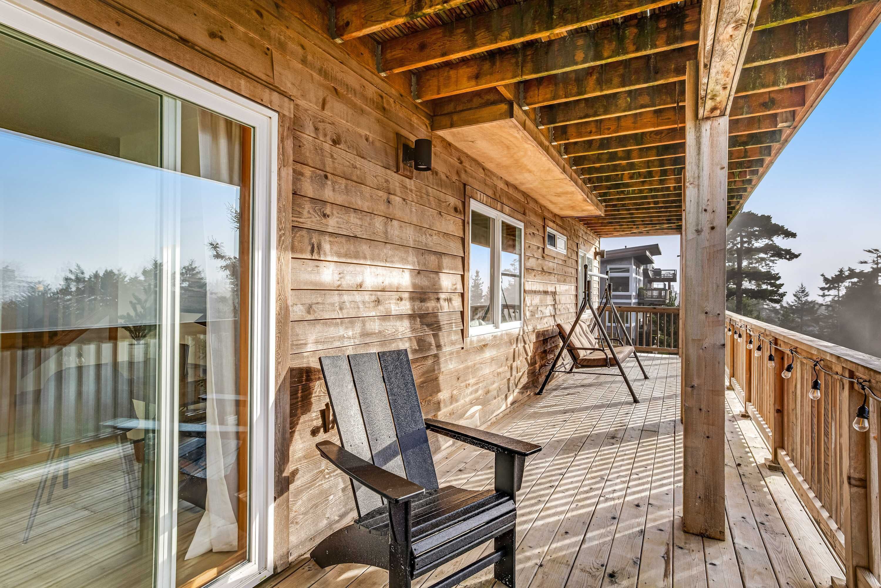 A wooden deck with a glass door leading to a room, a chair, and a railing with lights.