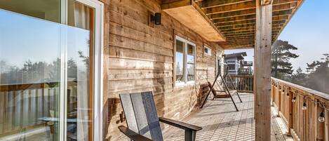 A wooden deck with a glass door leading to a room, a chair, and a railing with lights.