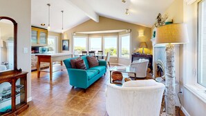 Ein geräumiges Wohnzimmer mit einem türkisfarbenen Sofa, einem weißen Sessel und einem Essbereich mit Tisch und Stühlen.