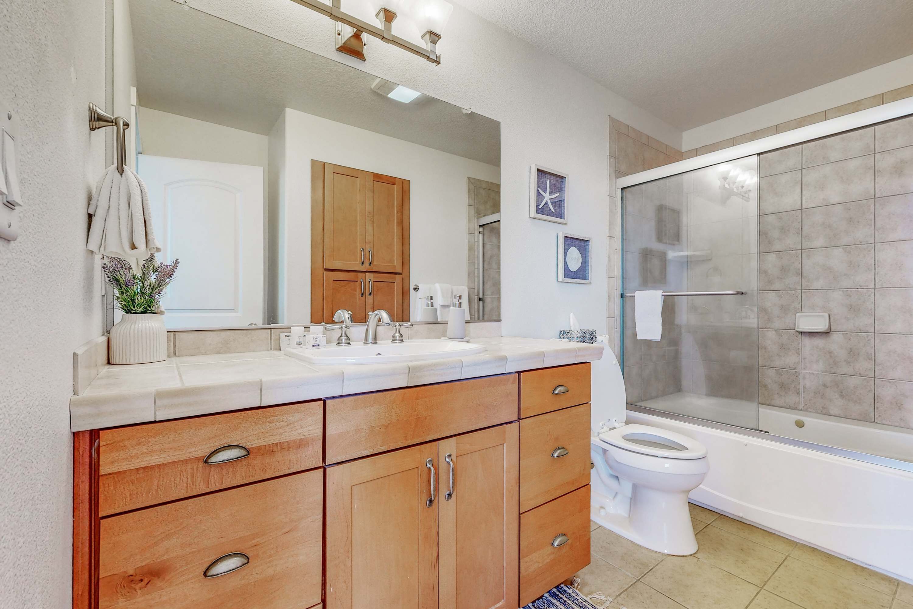 Une salle de bain avec un meuble-lavabo en bois, un grand miroir, un lavabo blanc, des toilettes et une douche à parois de verre.