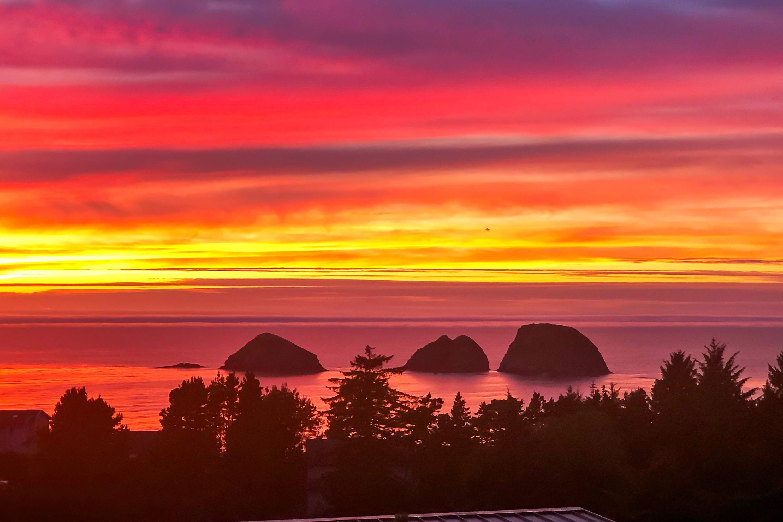 A sunset over a body of water with three prominent landforms in the distance.
