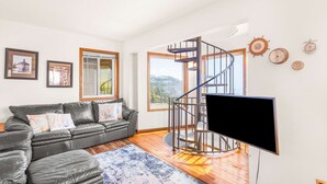 Ein modernes Wohnzimmer mit einer schwarzen Ledersofa, einem Flachbildfernseher, einer Wendeltreppe und großen Fenstern mit Blick ins Freie.