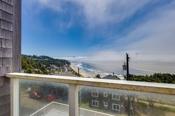 Een balkon met uitzicht op een strand en de oceaan, met een heldere lucht en een verre kustlijn.
