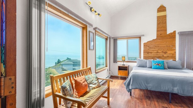 Ein Schlafzimmer mit großem Fenster, einem Holzkopfteil, einem Bett mit Kissen, einer Bank und einem Nachttisch.