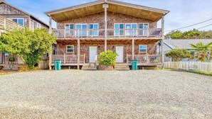 A two-story building with a wooden facade, multiple balconies, and a gravel driveway. - Large Sunny Duplex with Ocean Views and Nearby Beach Access Dogs OK (Rockaway Beach)