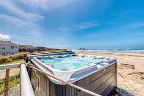 Un jacuzzi sur une plage, avec vue sur l’océan et une maison en arrière-plan.