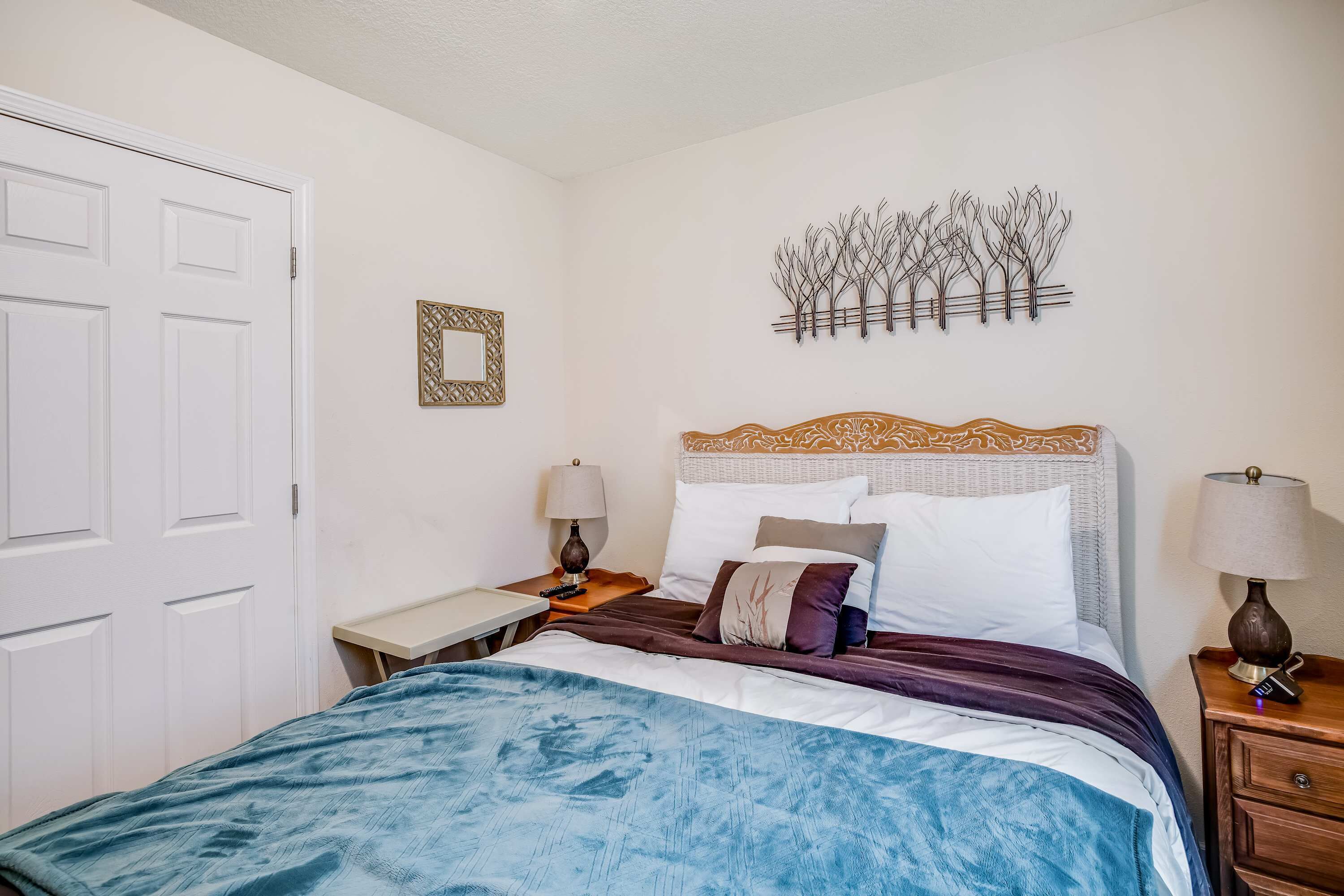 Une chambre à coucher bien rangée, avec un lit, des tables de chevet, une œuvre d’art accrochée au mur et une porte.