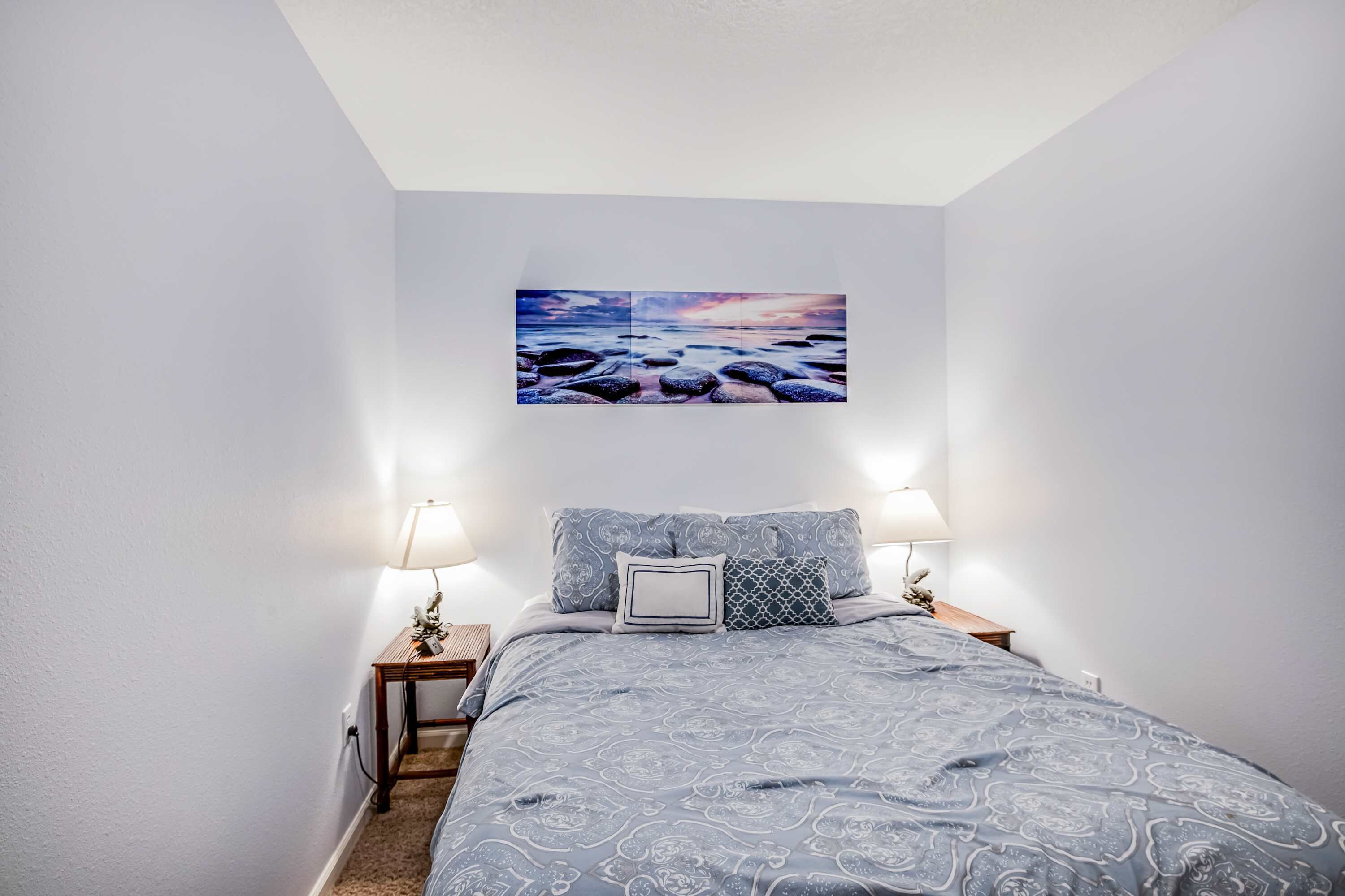 Une chambre à coucher avec un lit, deux tables de chevet, deux lampes et un tableau accroché au mur.