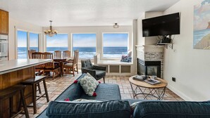 Tilava olohuone, jossa on suuri ikkuna, josta avautuu näkymä merelle, takka, televisio ja ruokailutila, jossa on puuhuonekaluja.