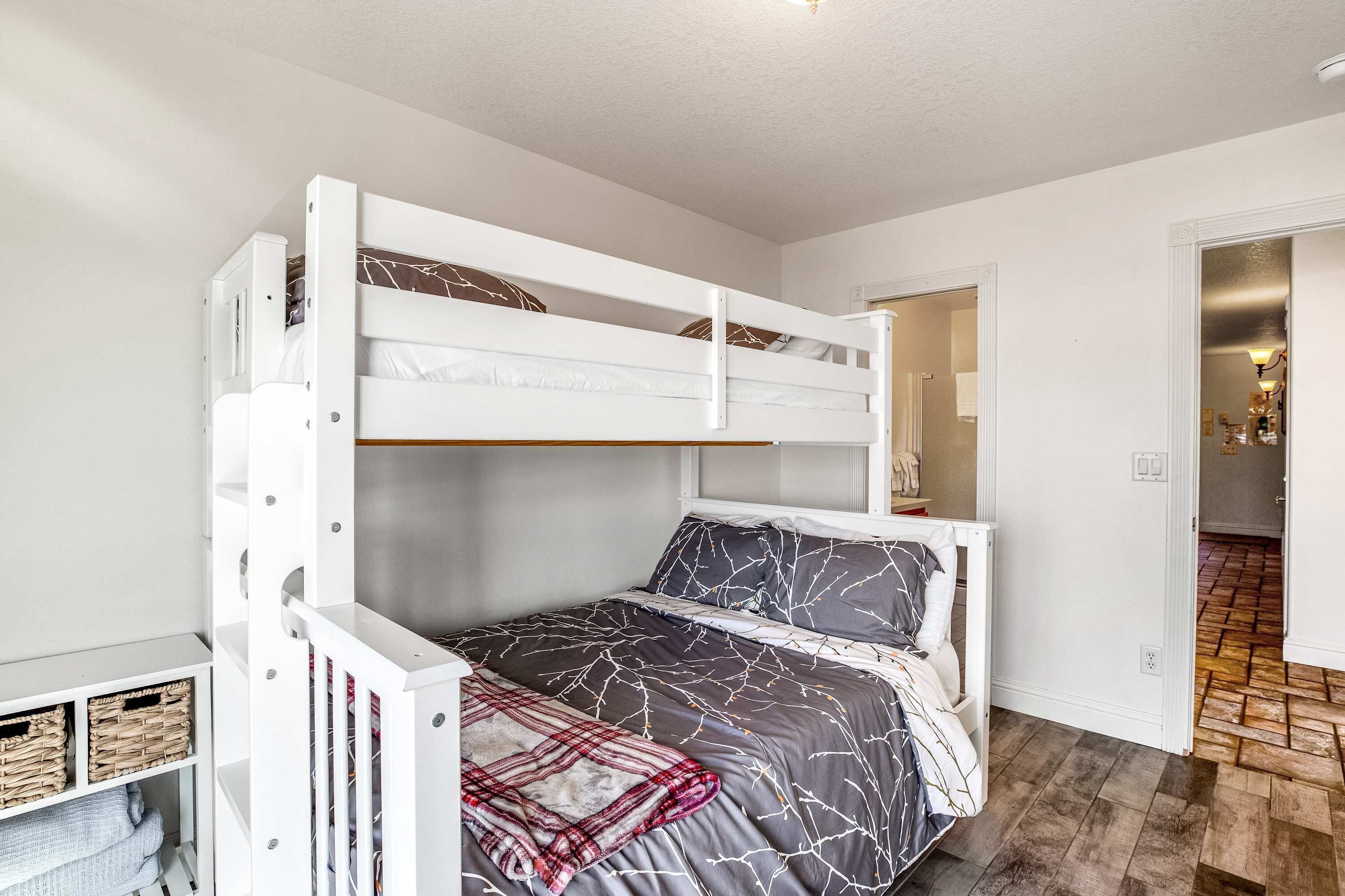 Ein Stockbett mit weißem Gestell, grau-weißer Bettwäsche und einer roten Karo-Decke.