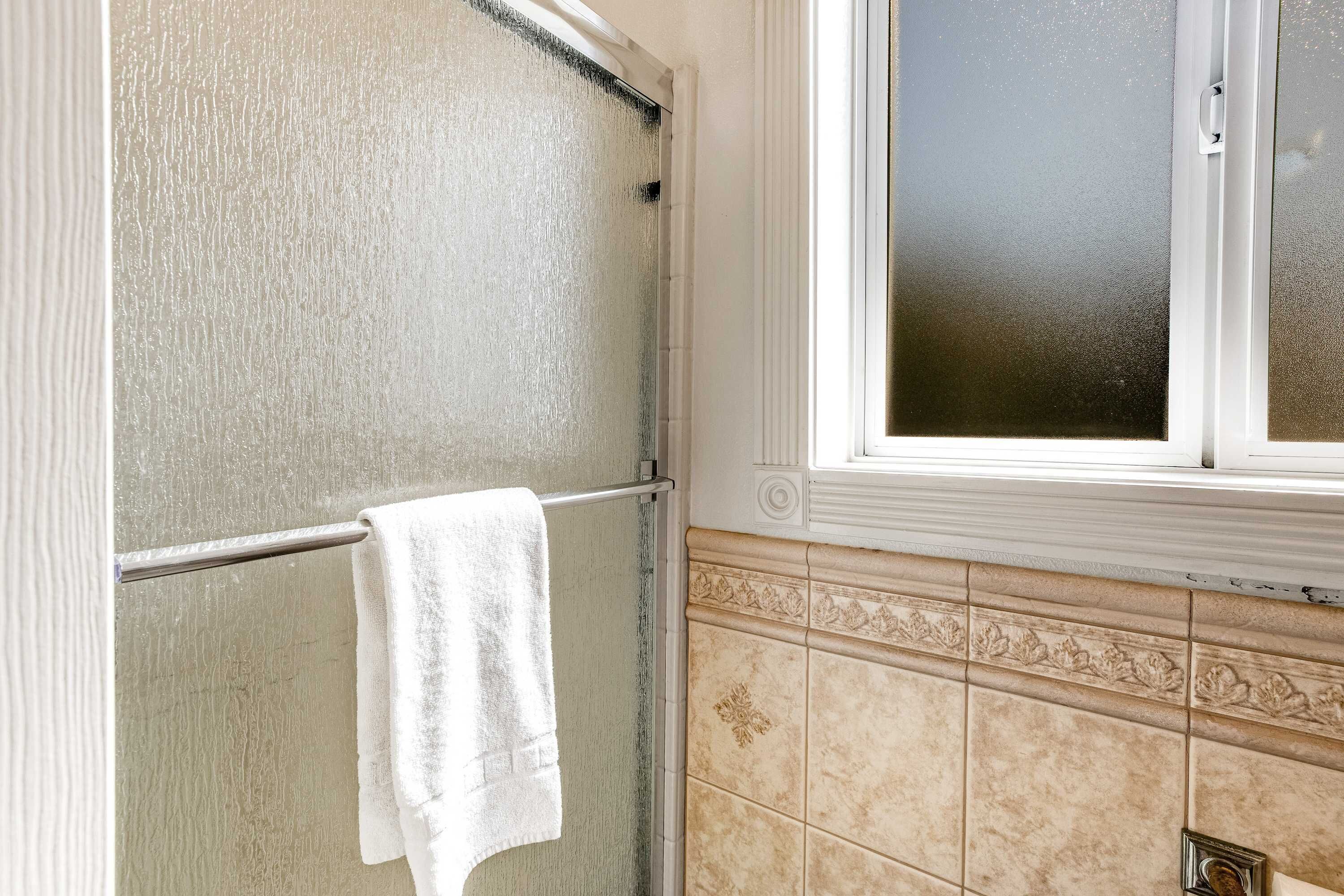 Ein Badezimmer mit Duschabtrennung aus Glas, einem Handtuch auf einem Halter und einem Fenster mit satiniertem Glas.