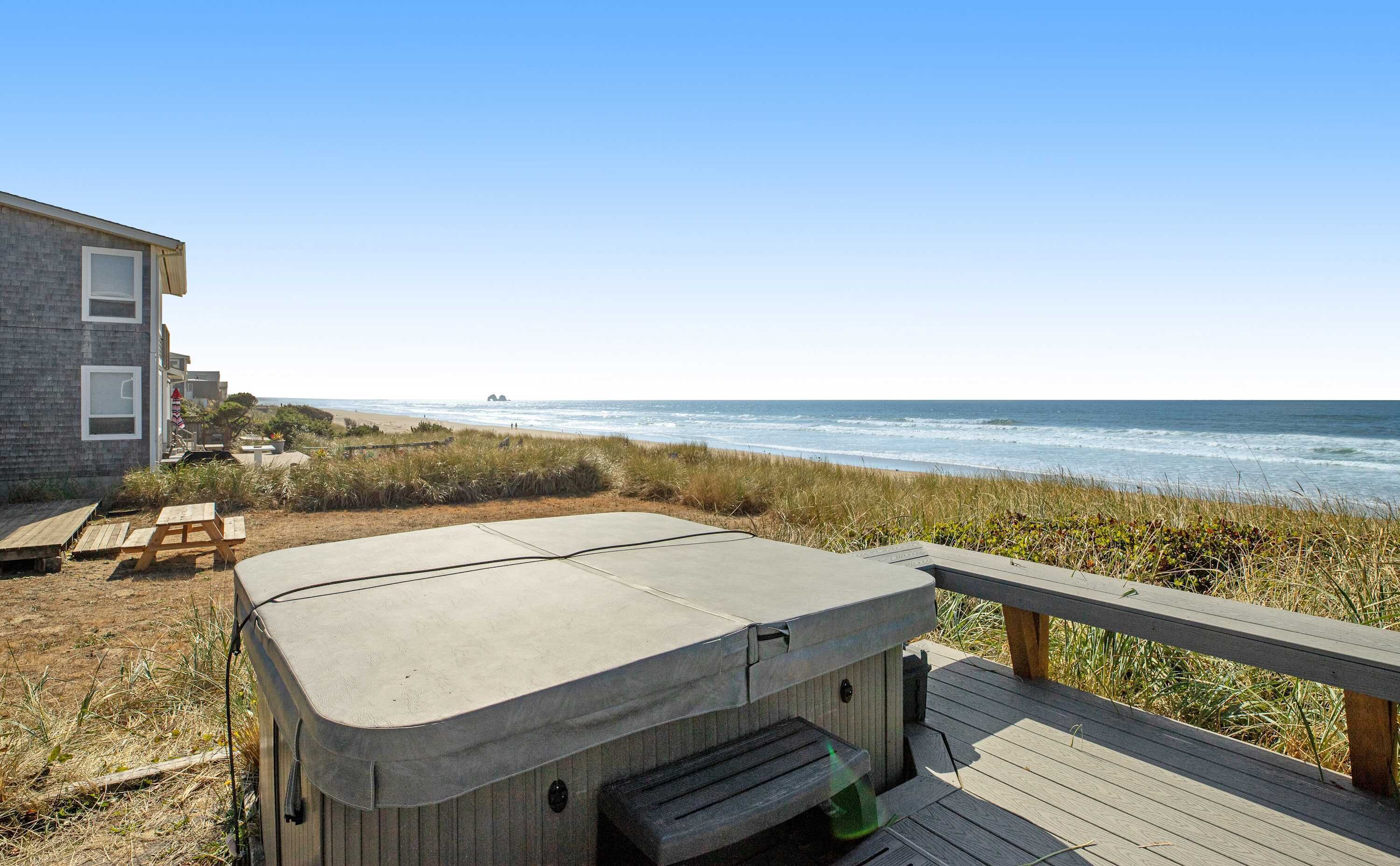 Un jacuzzi sur une terrasse en bois donnant sur une plage, avec une maison en arrière-plan.