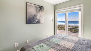 A bedroom with a large bed, a view of the ocean through a sliding glass door, and a painting on the wall. - Charming dog friendly waterfront beach home with lovely patio (Rockaway Beach)