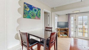 Een eethoek met een houten tafel en stoelen, een televisie op een dressoir en een kleurrijk schilderij aan de muur.