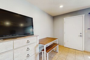 Ein Zimmer mit einem Flachbildfernseher auf einer Holzkommode, einer weißen Tür und einem gefliesten Boden.