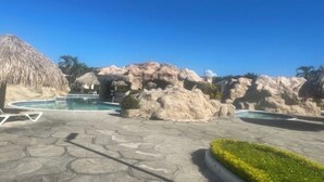 A pool area with a thatched-roof structure, large rocks, and a clear blue sky. - A homely villa at the beach (Trujillo)
