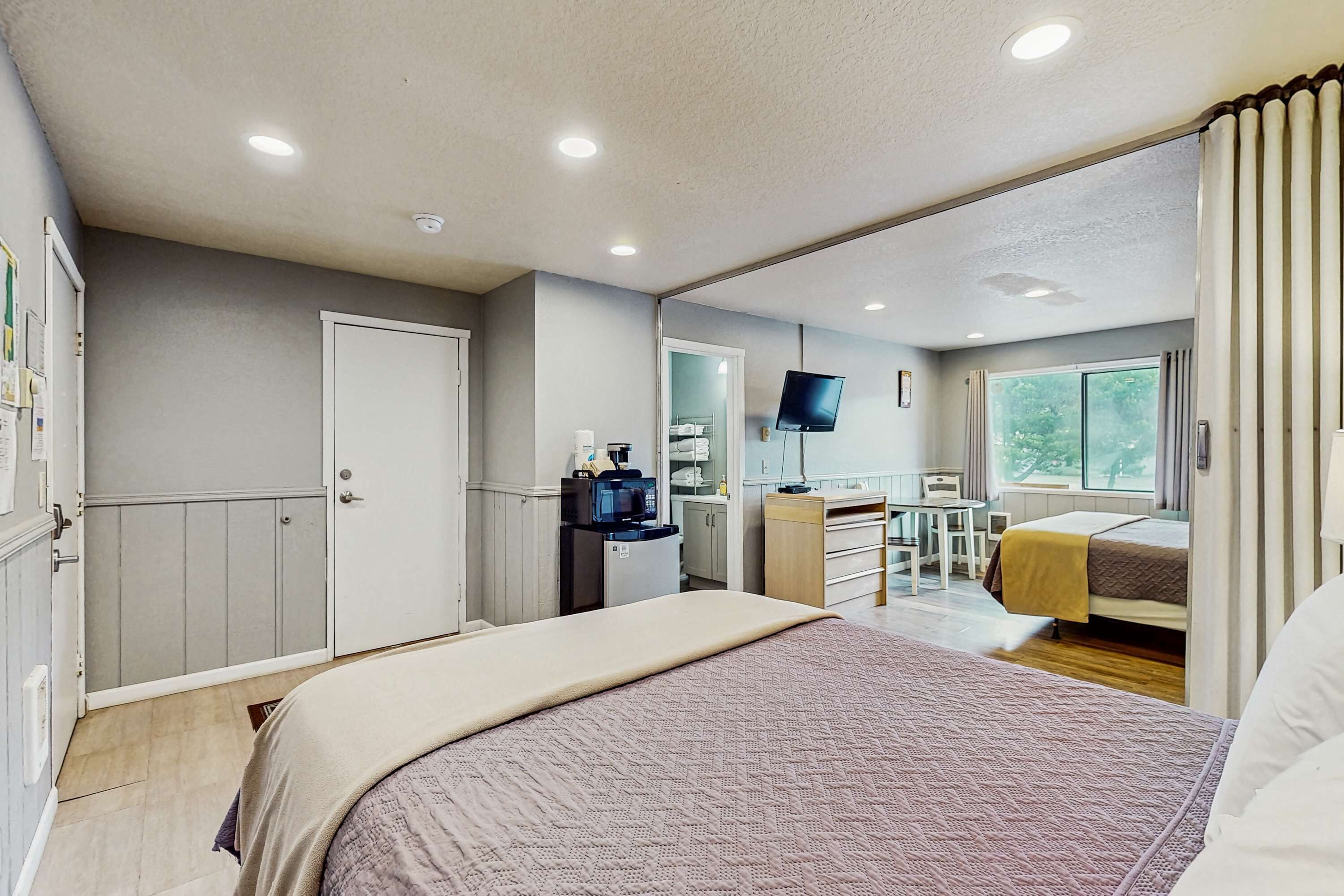 A bedroom with a bed, a desk with a computer, a television, and a window with curtains.