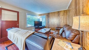 Ein Zimmer mit Massagetisch, Ledersofa, Fernseher und einem Fenster mit Jalousien.