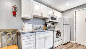 A kitchen with white cabinets, a microwave, a refrigerator, a sink, and a chair. - Six Dog Friendly Rooms with Full Kitchens and Kitchenettes Walk to the Beach (Rockaway Beach)