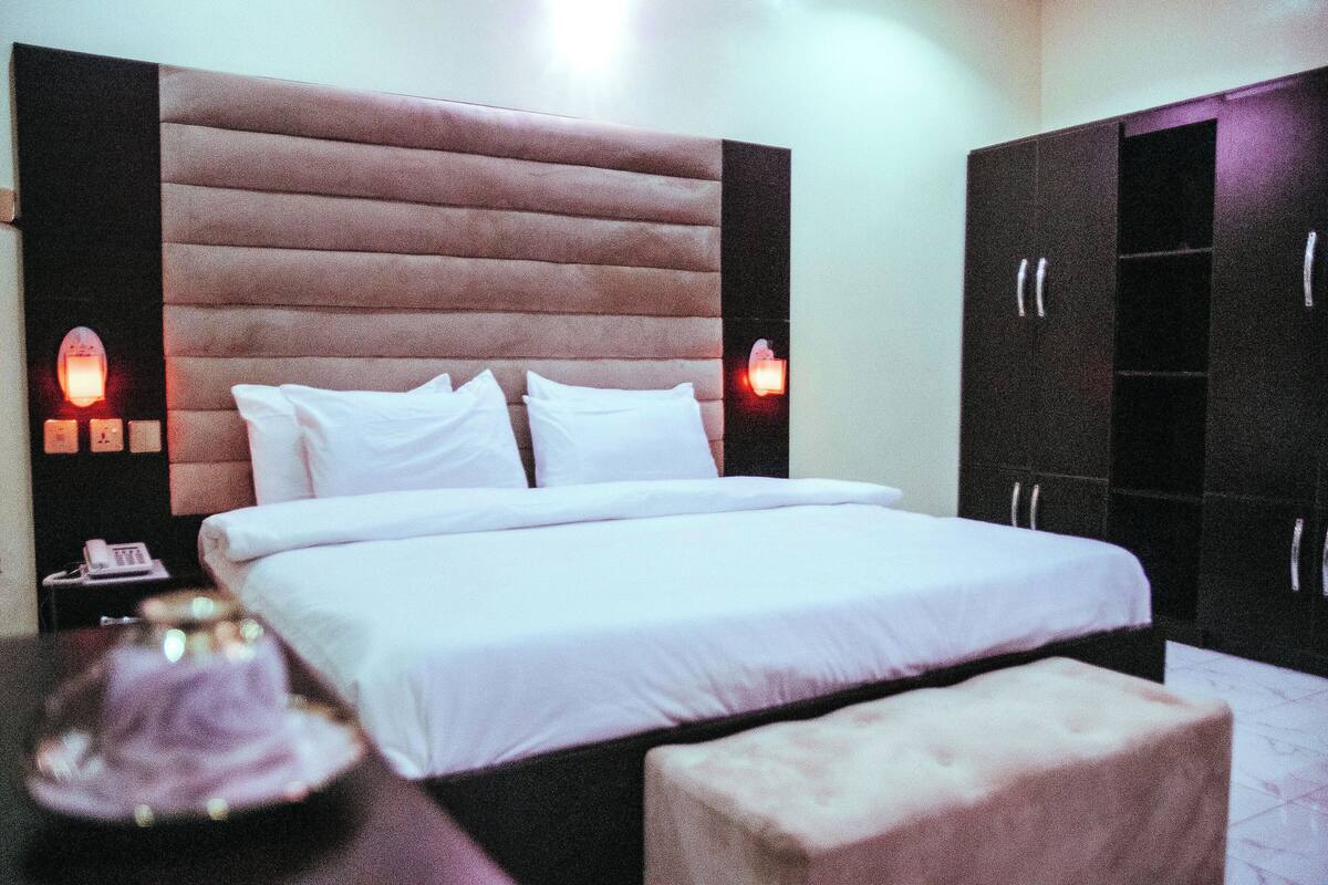 A hotel room with a large bed, a nightstand with a phone, and a wardrobe.
