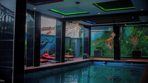 Une piscine intérieure ornée d’une fresque représentant un tigre et une cascade, entourée de colonnes noires et de fauteuils rouges.
