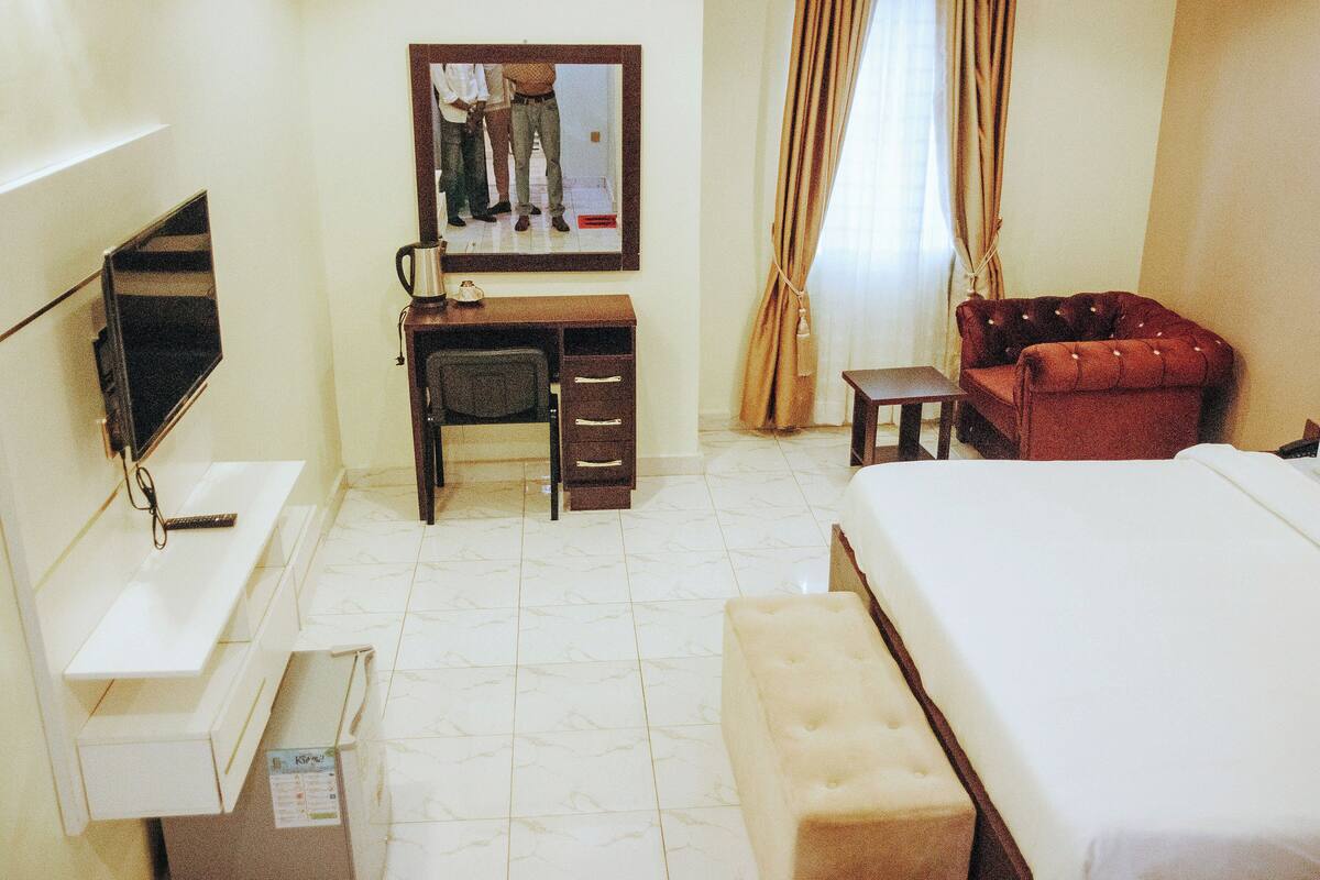A hotel room with a bed, a desk with a chair, a television, and a mirror.