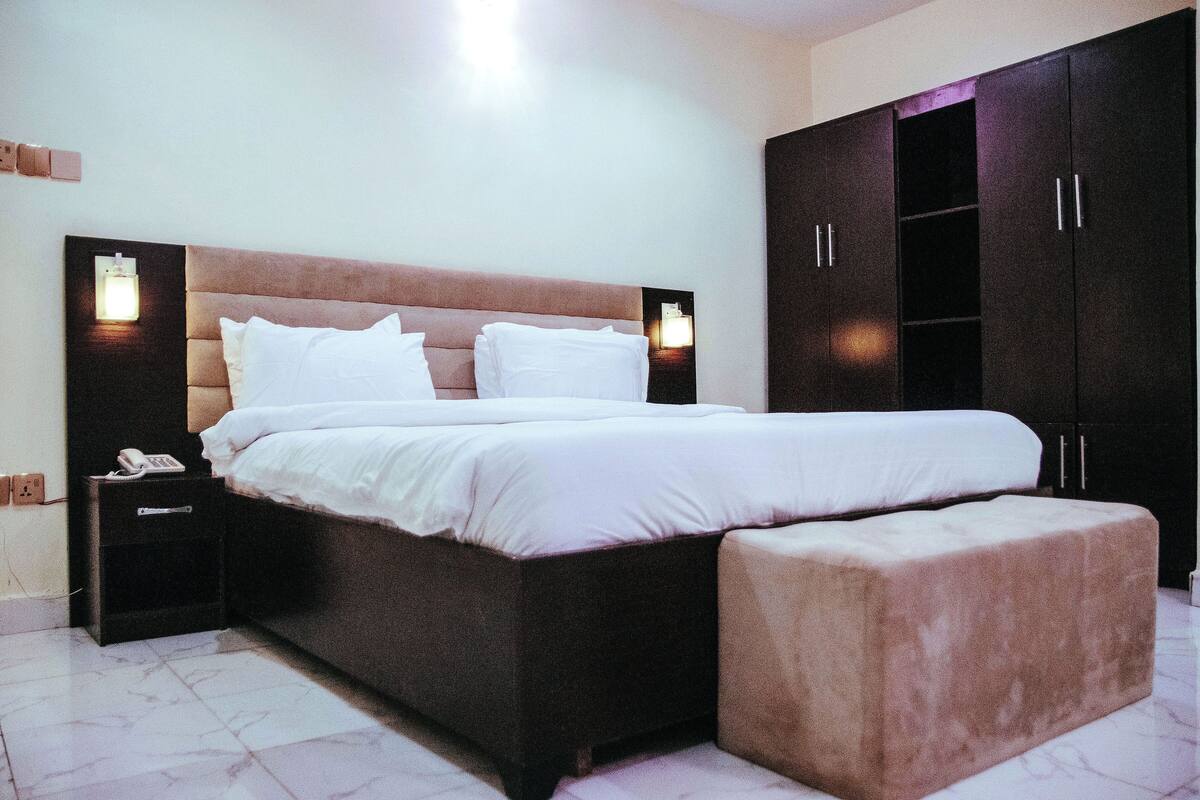 A neatly made bed with a headboard, a bedside table with a lamp, and a large wardrobe.