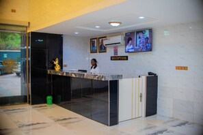 A reception area with a marble floor, a reception desk, a television, and a statue. - Golden Top Hotel (Enugu)